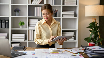 Attractive Asian businesswoman using her tablet and looking at a laptop screen