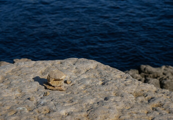 Stone pyramid. Balance. Dark blue sea background. Bright sunlight. Copy space.