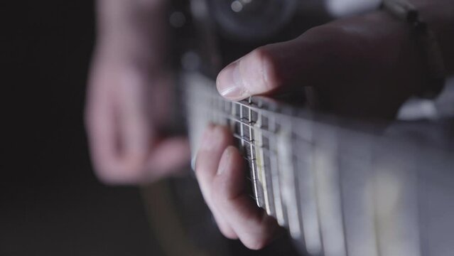 Looking down neck of electric guitar while man plays. Focus on frets, fingers.