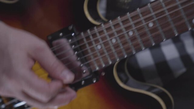 Man's hand strumming electric guitar, handheld close up, energetic feel.