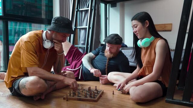 Group of backpacker multi-ethnicity tourists spend free time together by playing chess games, lifestyle Caucasian and Asian friends or couple take holiday vacation traveling stay in hostel in Thailand