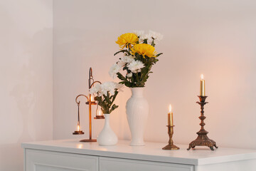chrysanthemums flowers in vases and burning candles on white interior