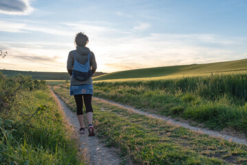 Woman walking at sunset between cereal fields