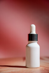 A white glass dropper bottle in hand on red background 