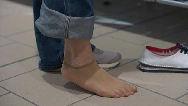 Close-up female leg with hand taking off oversize sandal keds indoors. Unrecognizable Caucasian adult woman trying on new shoes choosing footwear in shop