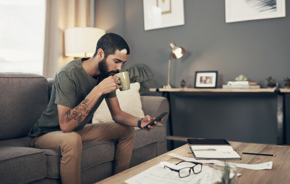 Tracking his spending with smart apps. a young man having coffee and using a smartphone while going through paperwork at home.