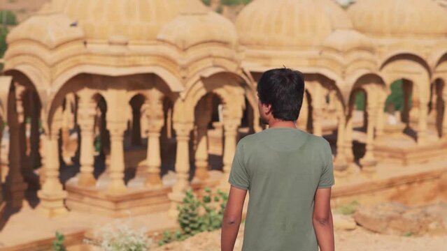 Rear view shot of an Indian man walking in front of the cenotaphs of Bada bagh in Jaisalmer, Rajasthan, India. Tourist walking in front of the old cenotaphs.
