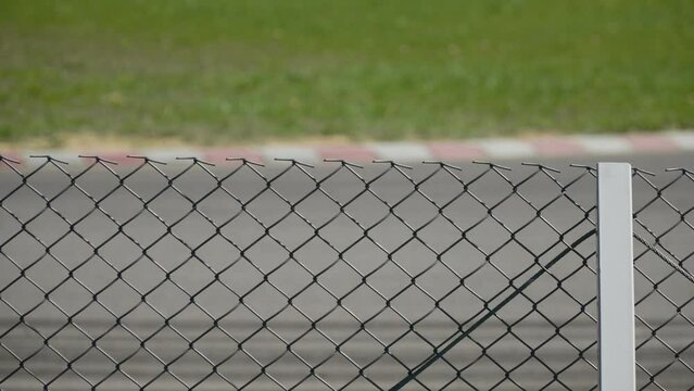 Safety fence made of metal mesh for racing asphalt ring track with curbs. Amateur racing stock car goes through corner in slow motion on sunny day. Generative AI