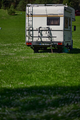 old school white camper parked on the grass by the lake. A vintage house on wheels in a sunny aura.