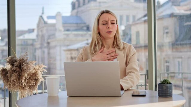 Overworked businesswoman experiences difficulty breathing and chest pain at work. Girl touching her chest, indicating possible breathing problems or a panic attack. Big bright office with city view.
