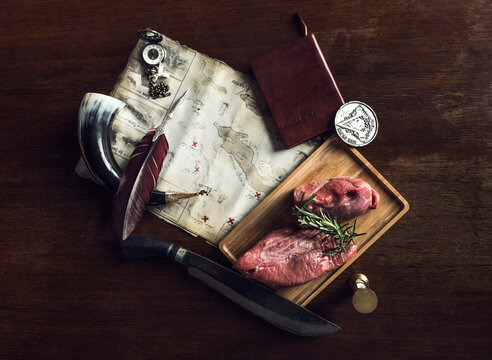 Raw meat on wooden board, map, and travel artefacts