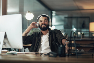 Turn the music up, keep your motivation levels up. a young businessman using a computer and headphones during a late night at work.