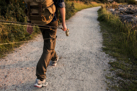 Man carrying fishing rod on dirt road