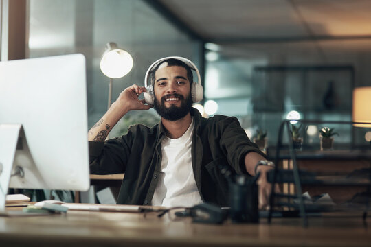 Turn the music up, keep your motivation levels up. a young businessman using a computer and headphones during a late night at work.