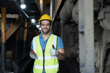 Portrait of male engineer worker maintenance locomotive engine, wearing safety uniform, helmet and gloves in locomotive repair garage. Male railway engineer working at repair train wheel in garage