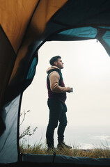 Nature invites us to be what we are. a young man drinking coffee while camping in the wilderness.