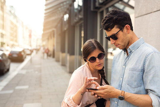 Couple Looking At Smart Phone On Sidewalk