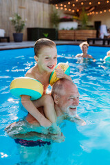 Grandfather with his grandson having fun together when playing in the swimming pool at backyard.