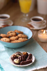 Fototapeta na wymiar Plate of chocolate pralines, bowl of cookies, cups of tea, glasses of juice and lit candles on the table. Selective focus.