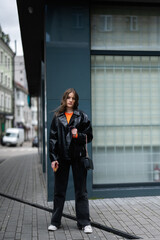 Young lady in leather jacket stand in urban city with credit card in hand.