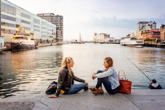 Two female friends sitting on waterfront and talking