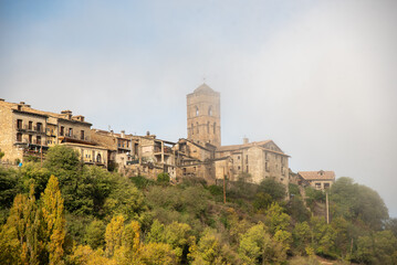 Obraz premium Panoramic view of the touristic village of Ainsa in Huesca surrounded by a natural landscape with its church on top of the hill and small brick and wooden houses during the sunset of a sunny day 