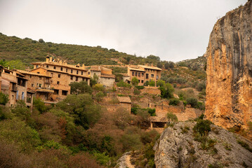 Fototapeta premium panoramic view of the touristy Aragonese village of Alquezar, with small brick houses on a rocky hill and a large church above on a cloudy day.