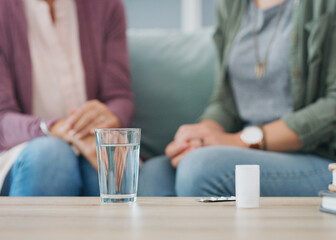 This is what senior healthcare looks like. two unrecognizable women sitting on the sofa with a pillbox and water in the living room.