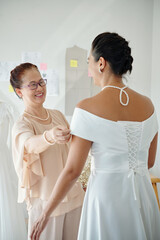 Naklejka premium Happy proud mother looking at her adult daughter in beautiful elegant wedding dress