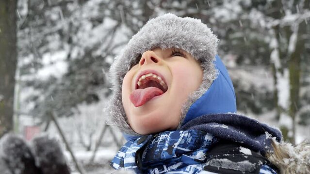Slow motion of young boy sticking out his tongue to catch snowflakes on a snowy day. Concept of playful winter activities