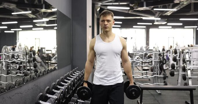 Man athlete carrying dumbbells in hands in gym 4k movie slow motion. Regular sports training concept
