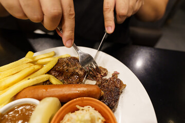 Man eating Grilled Meats stake from plate. hand holding knife and fork cutting grilled beef steak