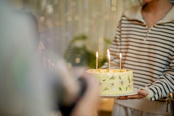 Cheerful friends enjoying home Birthday holiday party. Asian sister cheering drinking red wine celebrating with Birthday cake.