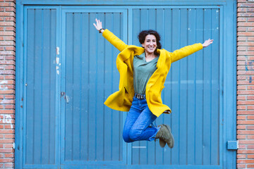 Smiling woman in a yellow coat jumping with energy