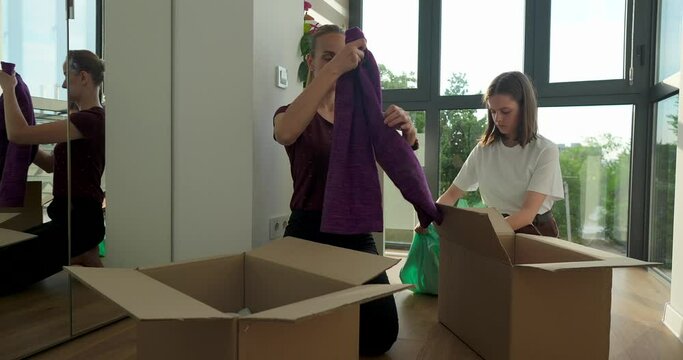 Mother and daughter sitting on floor and packing clothes in cardbox at home. Generative AI