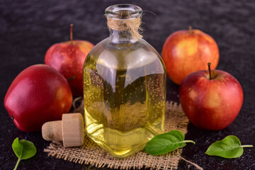 Apple cider vinegar and fresh apple on a black background.
