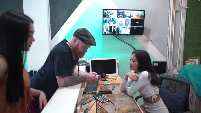 Beautiful young female receptionist sitting at counter welcoming new customer. Caucasian and Asian tourist register or check in at hostel. lifestyle backpacker traveling low cost expenses concept.
