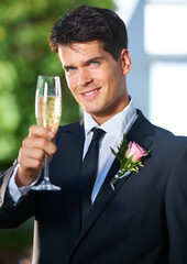 Toasting to a great day. Portrait of a handsome young groom toasting the camera with champagne.