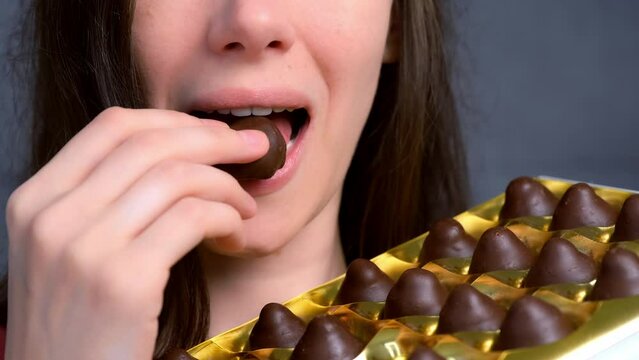 Mouth of woman is eating chocolate candies from box smelling them before it and smiling. Box of chocolates sweets set. Lots of truffles in a gift box. Bad habits, eating sweets.