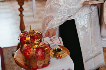 Priest holds two golden rings against background of wedding crowns during Wedding ceremony in Orthodox Ukrainian church.
