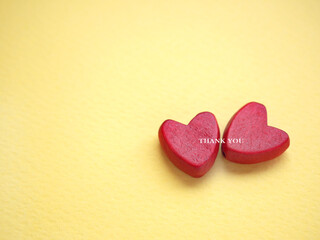 The words thank you message and two red heart on the yellow paper background. top view, flat lay with copy space. Greeting card