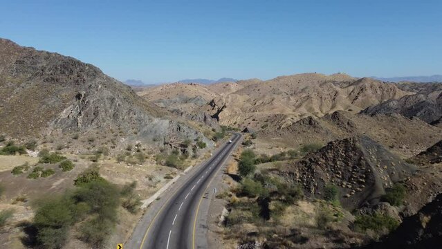 Aerial drone forward moving shot over truck driving along winding RCD Road through mountain range in Balochistan on a sunny day.