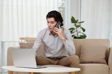 Businessman talking on phone when checking documents on laptop screen