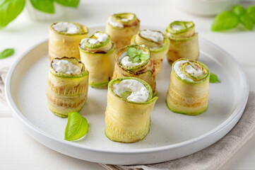Zucchini appetizer rolls with cream cheese, garlic and herbs on a plate on a white wooden background. Selective focus.
