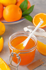 Orange marmalade or orange jam in glass jar with fresh fruits on a gray background. Copy space.