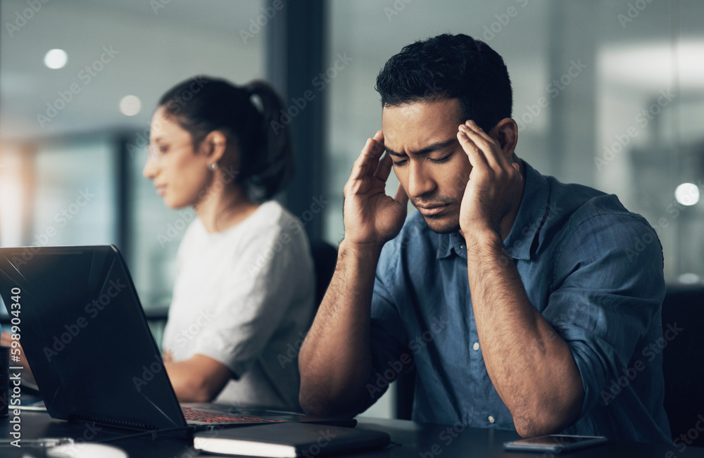 Poster well see in the end. a young man suffering from a headache while using a laptop in a modern office.