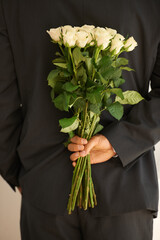 Ready to surprise that special someone. Cropped image of a young man in a suit holding a bunch of roses behind his back.