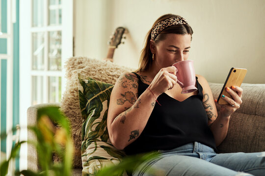 Do downtime your way. a young woman having coffee and using a smartphone on the sofa at home.
