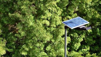 Lighting pole with photovoltaic panel and LED lamp lights with green background on in garden. Production of renewable energy concept.
