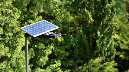 Lighting pole with photovoltaic panel and LED lamp lights with green background on in garden. Production of renewable energy concept.